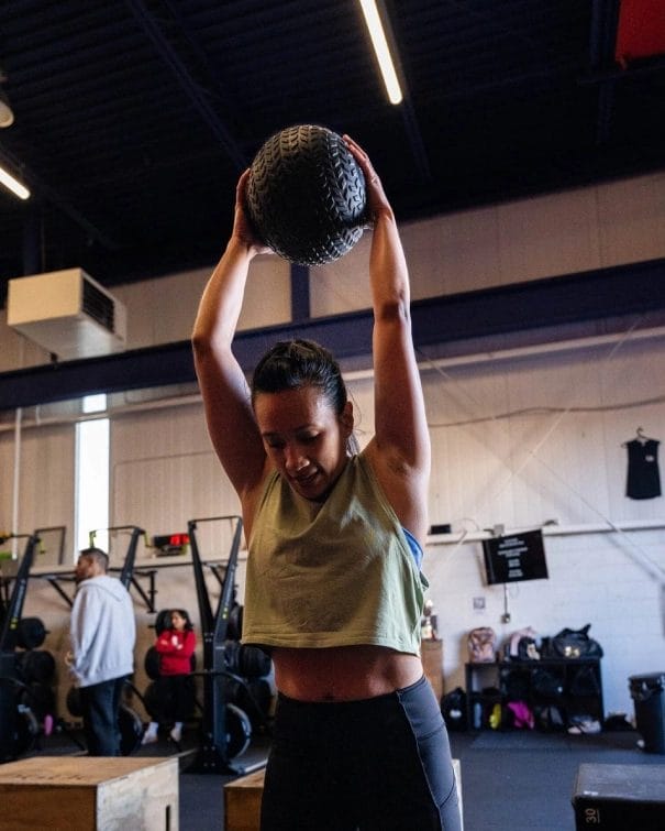 Woman lifting medicine ball over head at BURN training at Energia Athletics